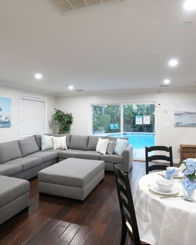 Open-plan living and dining room with gray sectional sofa, dining table, and sliding glass doors overlooking swimming pool