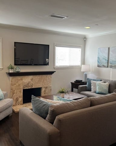Bright living room with beige sectional sofa, stone fireplace with mounted TV, and abstract wall art