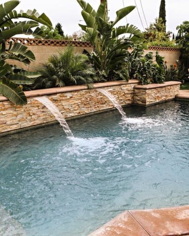 Backyard swimming pool with stone waterfall features, surrounded by tropical plants and Adirondack chairs
