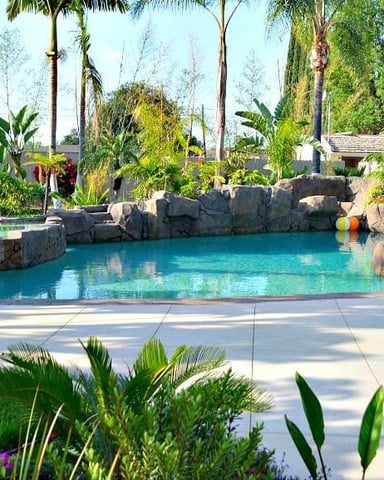 Resort-style lagoon pool with turquoise water, rock features, palm trees, and lounge chairs in landscaped backyard