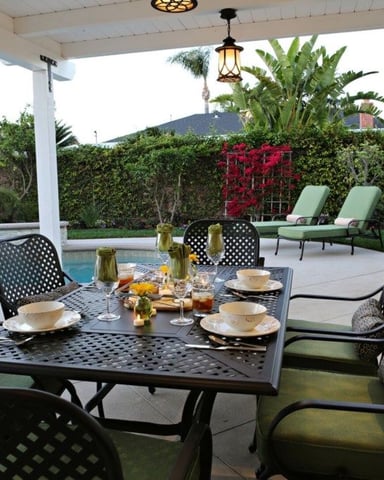 Covered patio with dining table set for six, pool, lounge chairs, and manicured hedges with mountain view