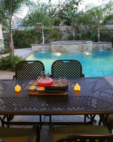Patio dining table with lit candles overlooking illuminated swimming pool surrounded by tropical plants and stone features