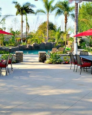 Backyard patio with red umbrellas, seating areas, pool, and tropical landscaping with palm trees