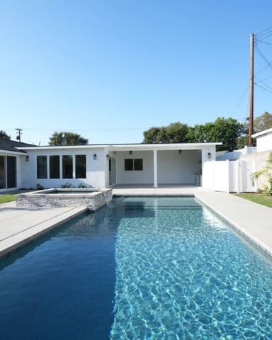 Modern white house with rectangular swimming pool, concrete deck, and palm trees in landscaped yard