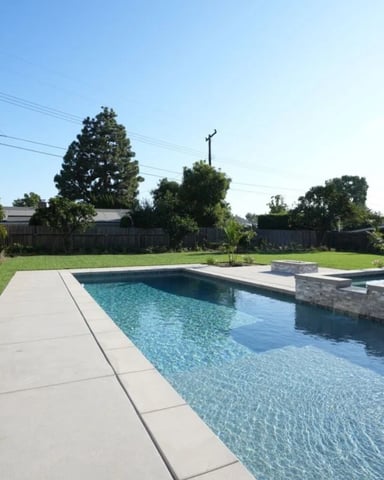 Backyard with rectangular swimming pool, concrete deck, spa, manicured lawn, and neighboring houses under clear sky