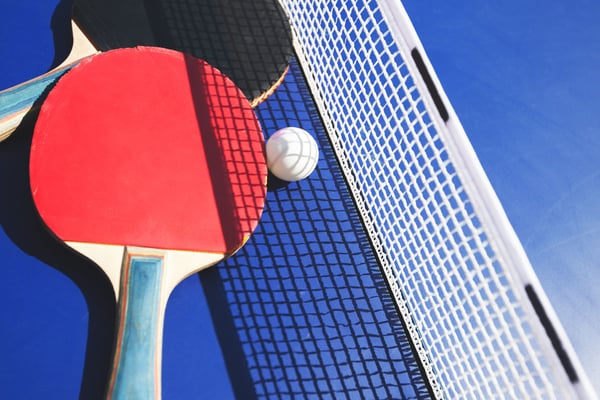 Ping pong paddle with red face and white ball near net against blue background