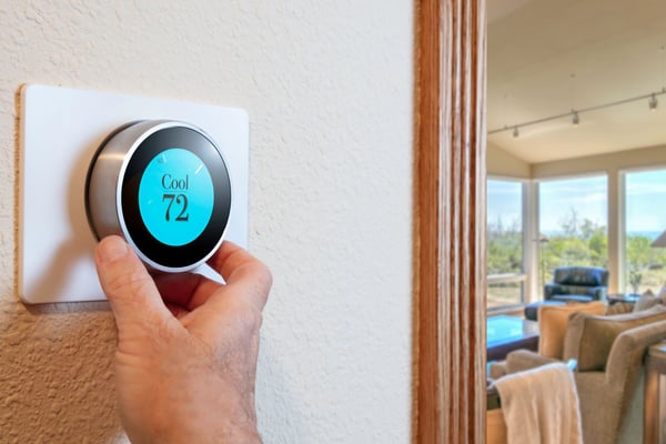 Hand adjusting smart thermostat set to 72 degrees, with living room and mountain view visible through open doorway