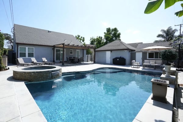 Backyard with large swimming pool, circular hot tub, modern gray house, lounge chairs, and palm trees