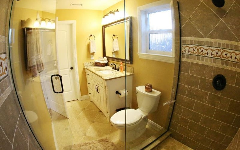 Bathroom with yellow walls, double vanity with mirrors, glass shower enclosure, and toilet