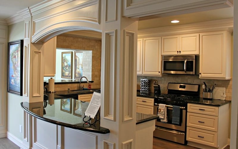 Cream-colored kitchen with black granite countertops, stainless steel appliances, and curved archway opening to dining area