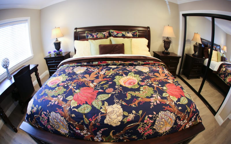 Master bedroom with dark wood bed, floral patterned comforter, yellow pillows, matching nightstands with lamps, and black mirror.
