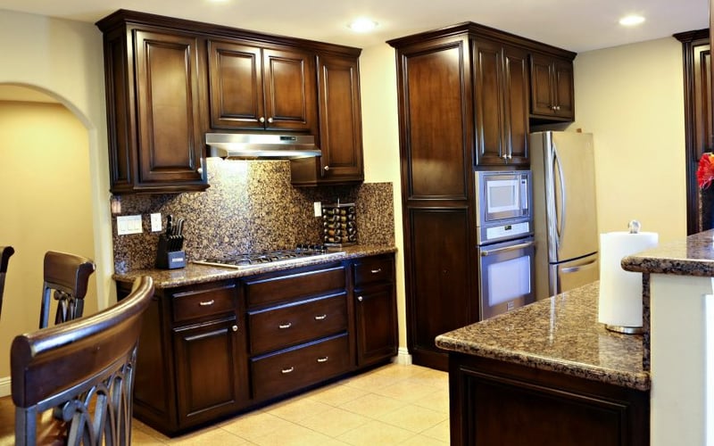 Kitchen with dark wood cabinets, granite countertops, granite backsplash, stainless steel appliances, and island with seating.