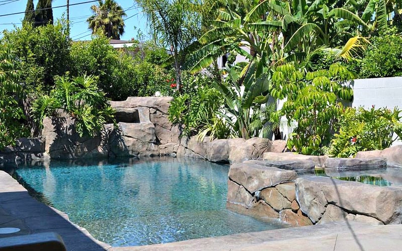 Resort pool with turquoise water, large boulders, tropical plants, and palm trees in background