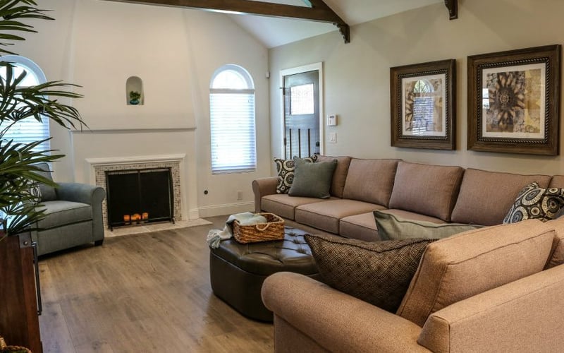 Spacious living room with vaulted ceiling, fireplace, tan upholstered sectional sofa, and framed artwork on walls