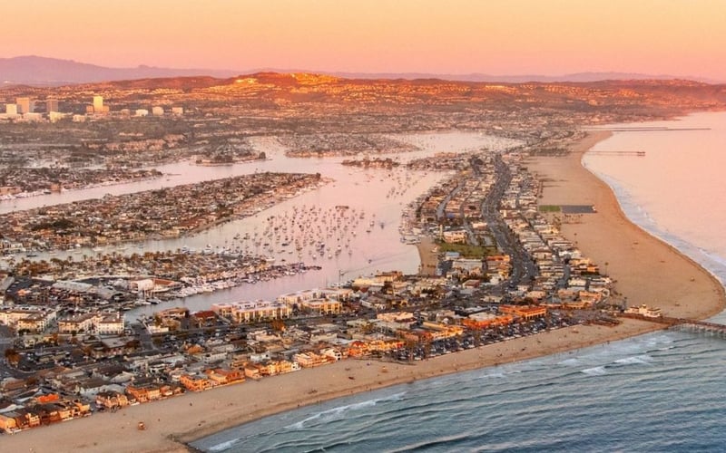Aerial view of coastal city at sunset with beach, pier, bay, and mountains in distance