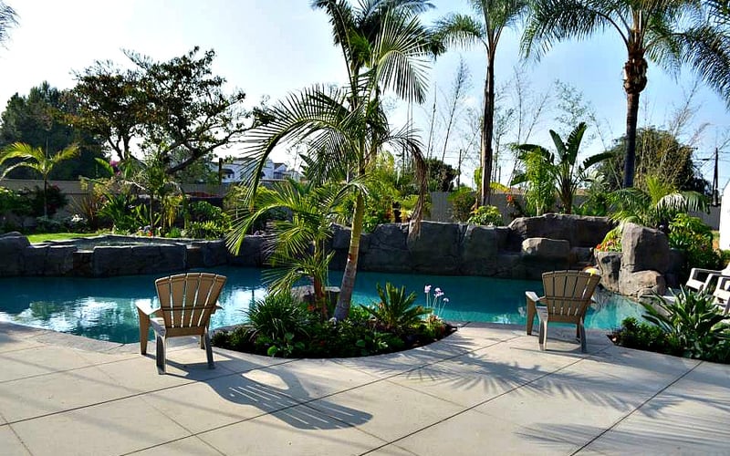 Resort pool with turquoise water, palm trees, lounge chairs, and stone waterfall feature