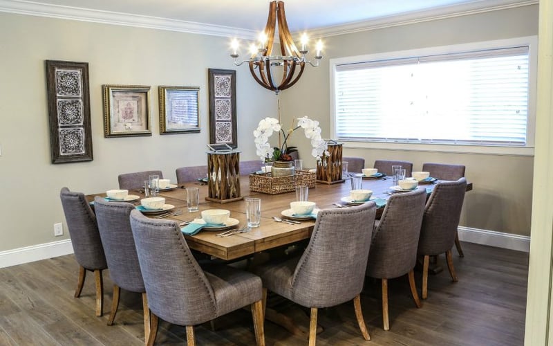 Formal dining room with oval wood table, gray upholstered chairs, wooden chandelier, and framed wall art